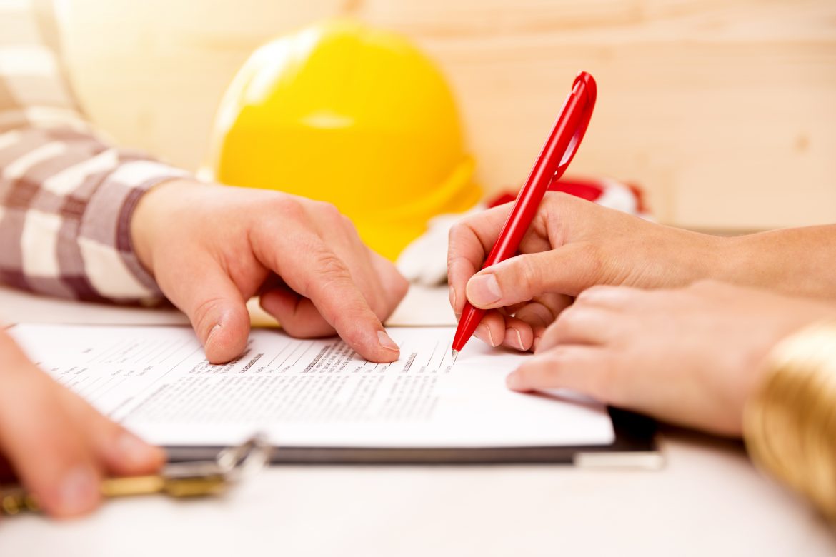 Close-up of a person signing a contract with a construction hardhat in the background
